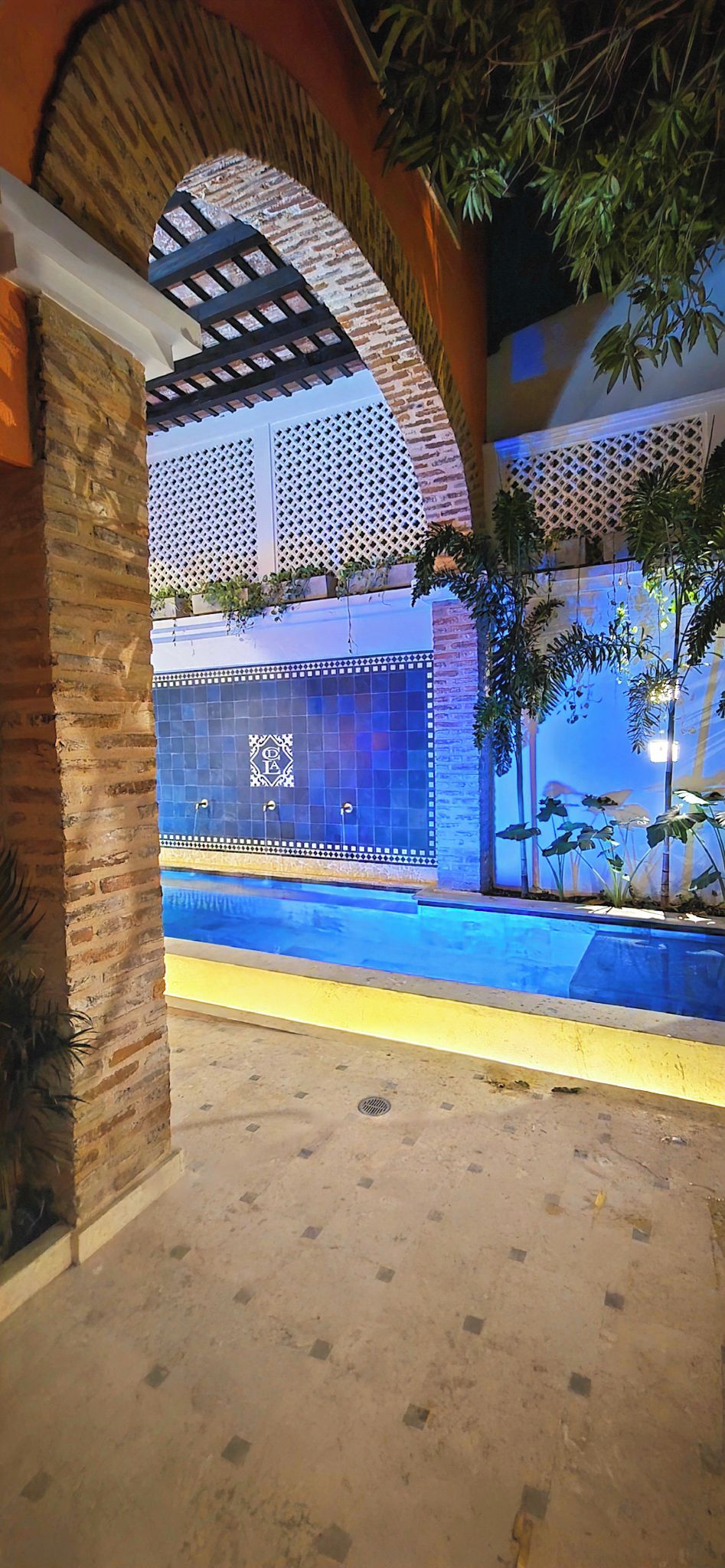 A pool area with a tiled wall, a brick archway, and potted plants.