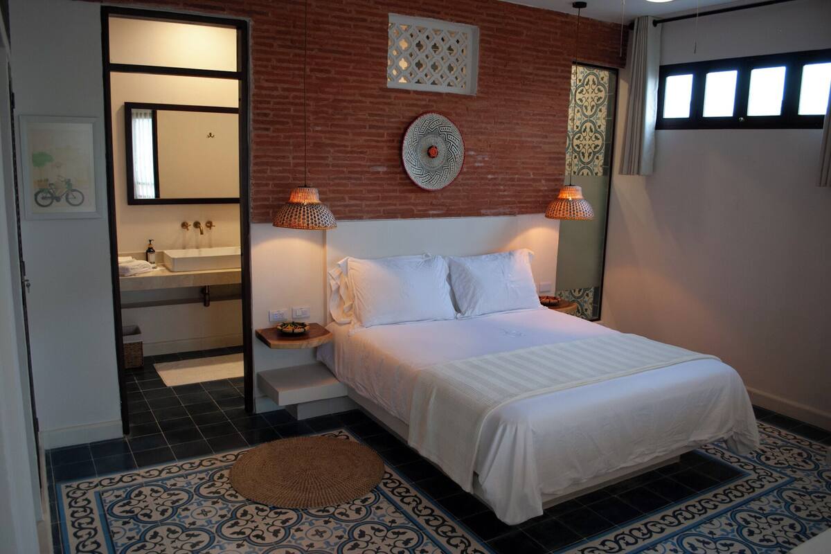 A bedroom with a bed, bedside lamps, a mirror, a sink, and a patterned floor.