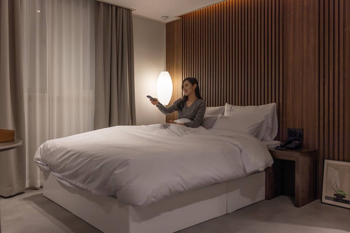 Una habitación de hotel moderna con una cama grande, una mesita de noche con teléfono y una lámpara de pared.