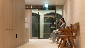 Un interior moderno con paneles de madera, una zona de recepción con puertas de cristal y un área de descanso con sillas de madera.
