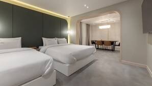 Una habitación de hotel moderna con dos camas, una zona de comedor con una mesa y sillas, y un espejo grande.