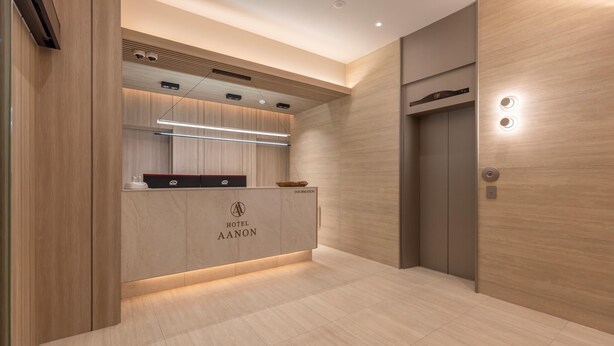 Zona de recepción de hotel con un mostrador de madera, una lámpara moderna y un panel de control en la pared.
