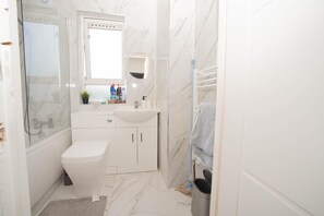 Bathroom features a glass-enclosed shower, toilet, sink, and towel rack.