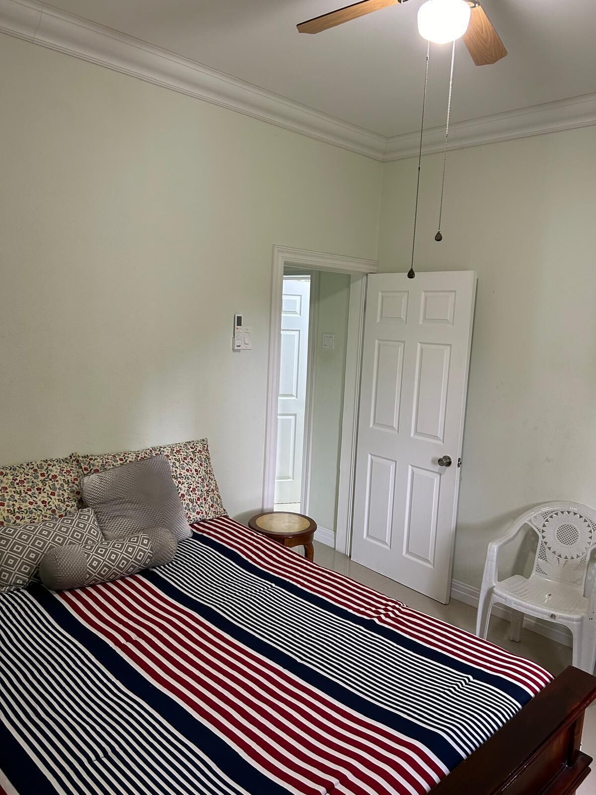 Une chambre à coucher avec un lit, un ventilateur de plafond, une porte blanche et une petite chaise blanche.