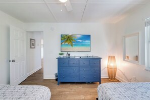 A bedroom with two beds, a dresser, a painting of a beach, and a lamp.
