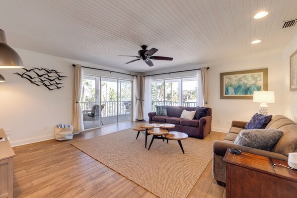 A spacious living room with a ceiling fan, a large window with curtains, a sofa set, and a coffee table.