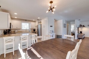 A modern kitchen with white cabinetry, a central island with bar stools, and a dining area with a large wooden table.