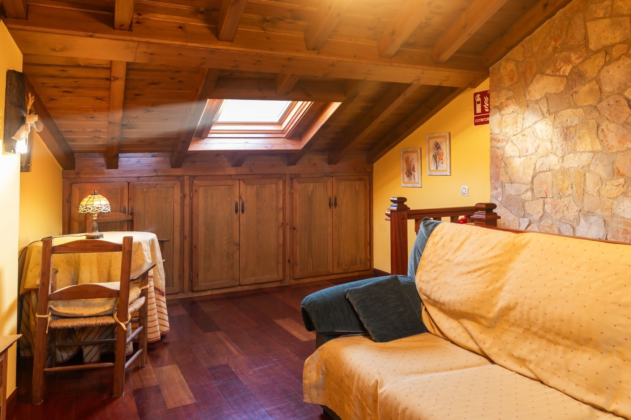 Une pièce chaleureuse avec des poutres en bois, un mur en pierre, une lucarne, une table à manger avec des chaises et un canapé.