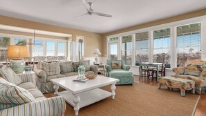 A spacious living room with striped sofas, a white coffee table, and a ceiling fan. - Discover your dream beach house with an amazing ocean view and lots of deck space on South Beach! (Bald Head Island)