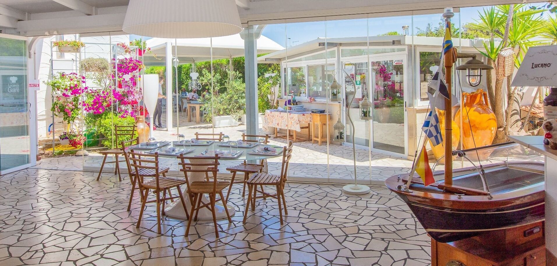 An outdoor dining area with a glass enclosure, wooden tables and chairs, and a decorative boat.