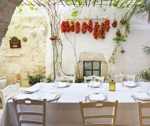 A table set for four with white tablecloths, white chairs, and a small potted plant on the table.