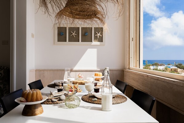 Une table à manger dressée avec de la nourriture et des boissons, une vue sur l’océan et un mur décoré d’étoiles de mer.