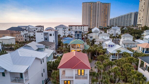 A coastal residential area with modern houses, a prominent red-roofed building, and a backdrop of high-rise buildings.