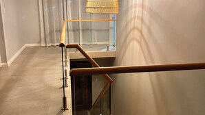 A modern interior with a glass railing, a wooden handrail, and a woven light fixture.