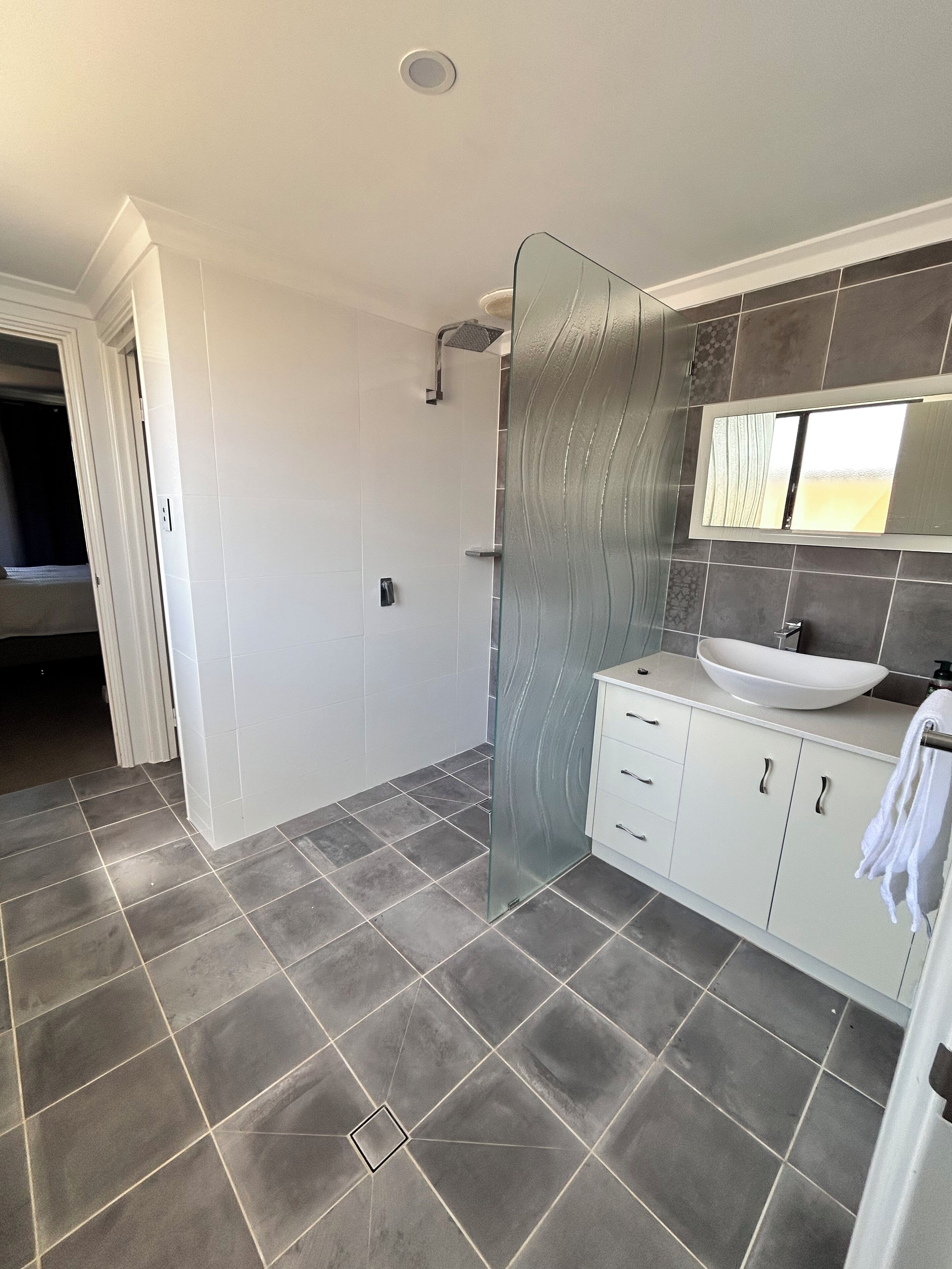 A modern bathroom with a glass shower enclosure, a white sink, and a vanity with drawers.