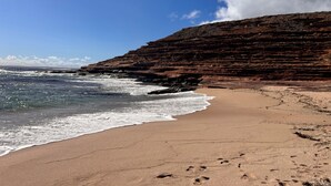 A beach with a rocky cliff and ocean waves.