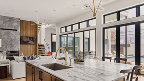 Eine moderne Küche mit Marmorarbeitsplatte, Holzschränken und einem großen Fenster mit Blick auf einen Pool.