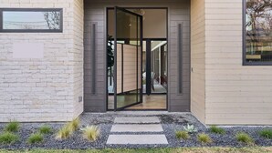 Ein moderner Eingangsbereich mit Glastür, einem Kiesweg und einem kleinen Garten.
