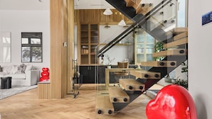 Ein modernes Interieur mit einer Holztreppe, einem Glastrennwerk und einem roten, herzförmigen Objekt.