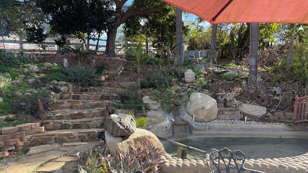 A patio area with stone steps, a small pond, and metal chairs.