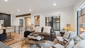 A modern living room with a brown leather sofa, a coffee table, and a dining area with a wooden table and chairs. - The Silver Buffalo Suite in Downtown Whitefish (Whitefish)