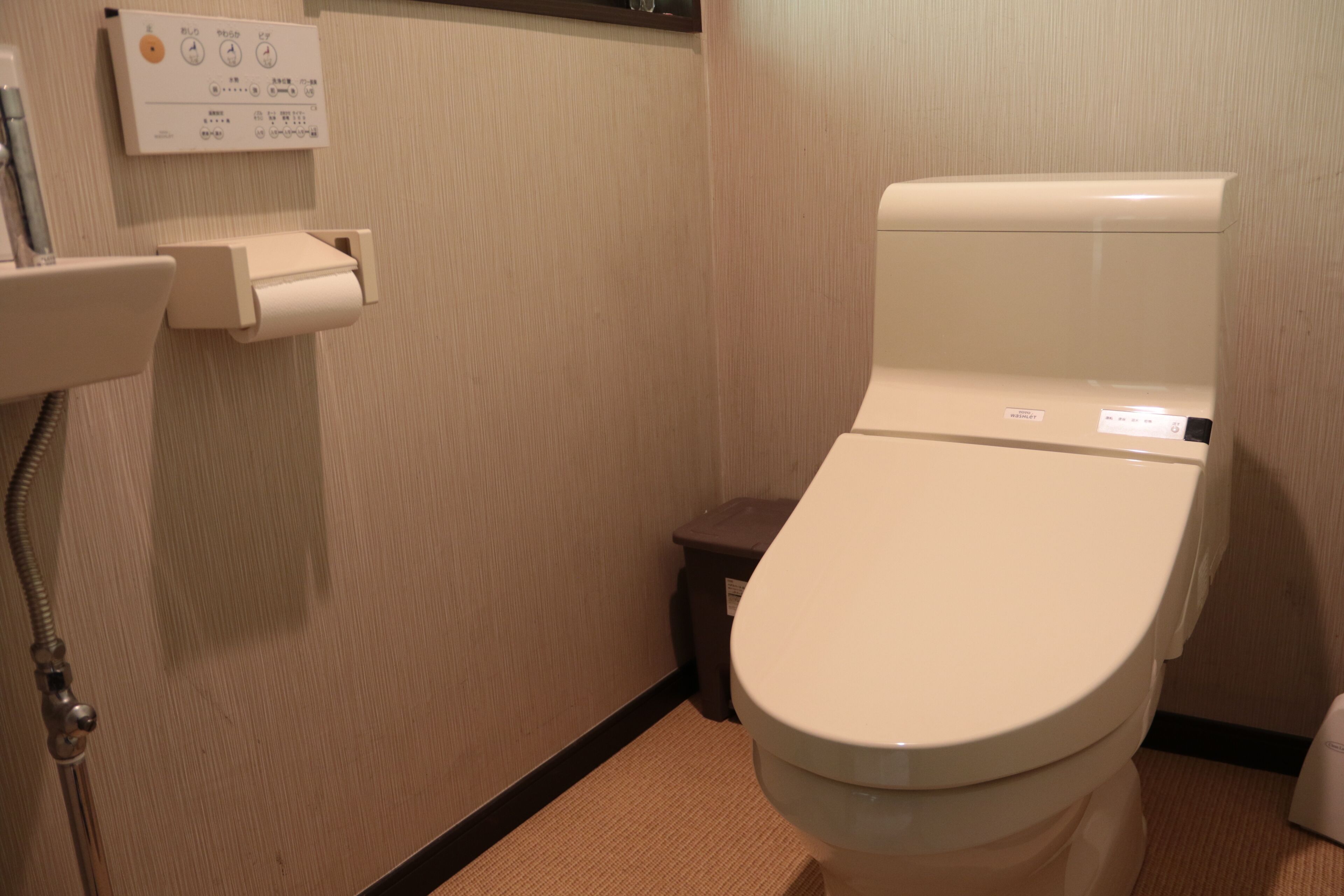 Un baño de hotel estándar con inodoro, dispensador de toallas de papel y secador de manos.