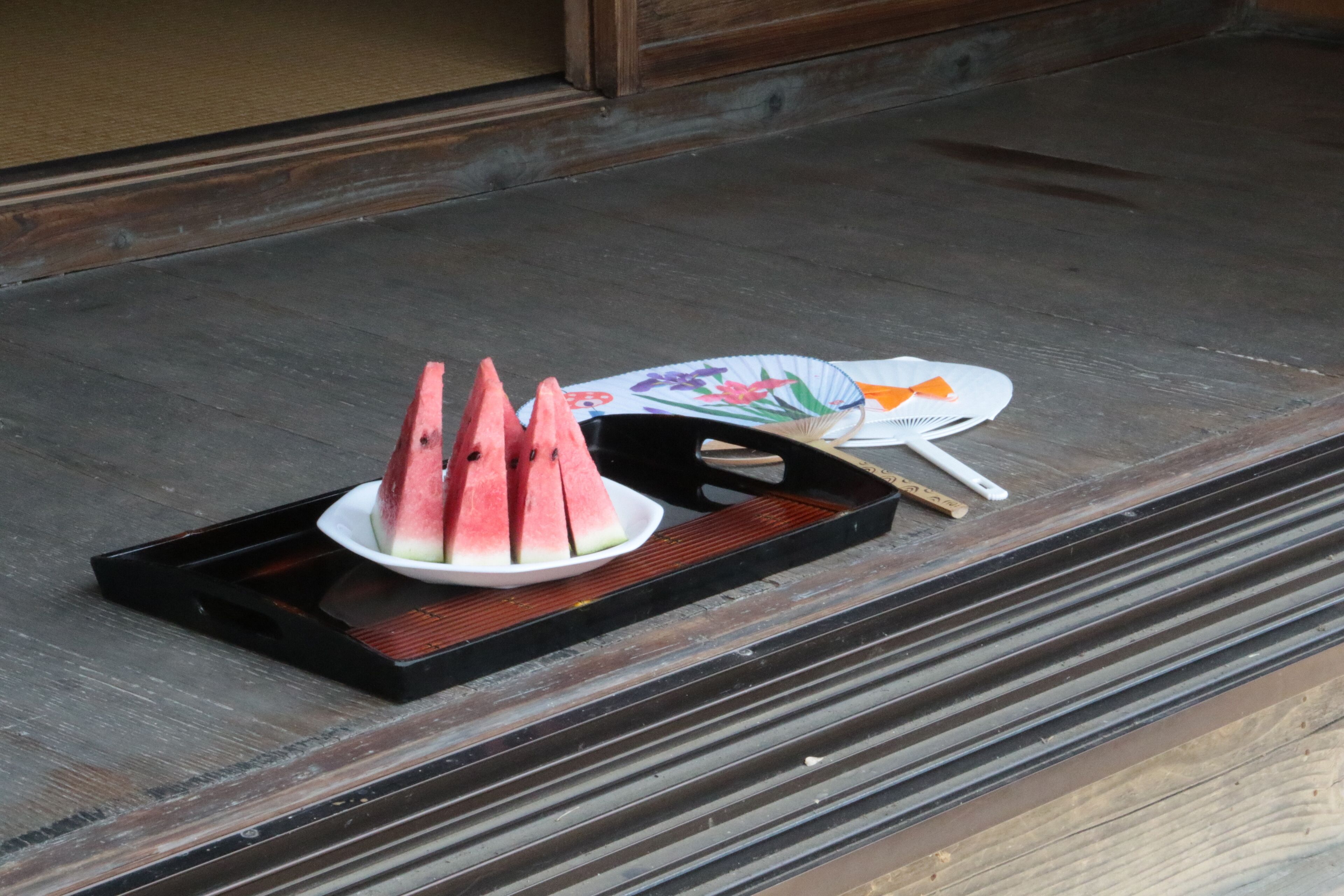 A tray with sliced watermelon and a fan on a wooden surface.
