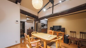 Zona pranzo con tavolo e sedie in legno, una televisione e una cucina sullo sfondo.