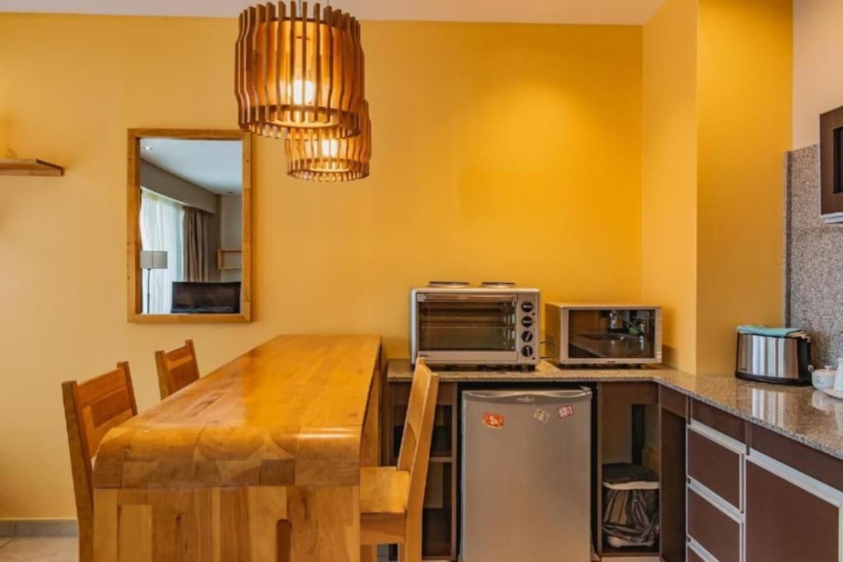 A compact kitchen with a wooden dining table, a built-in microwave, a toaster, and a refrigerator.