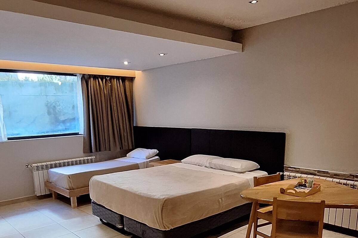 A modern hotel room with a large bed, a small table, and a window with curtains.