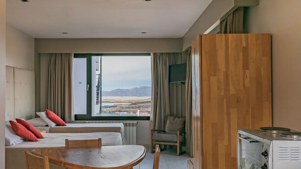 A hotel room with a bed, a dining table, chairs, a TV, and a view of the outdoors. - MIRALEJOS APART HOTEL (Ushuaia)