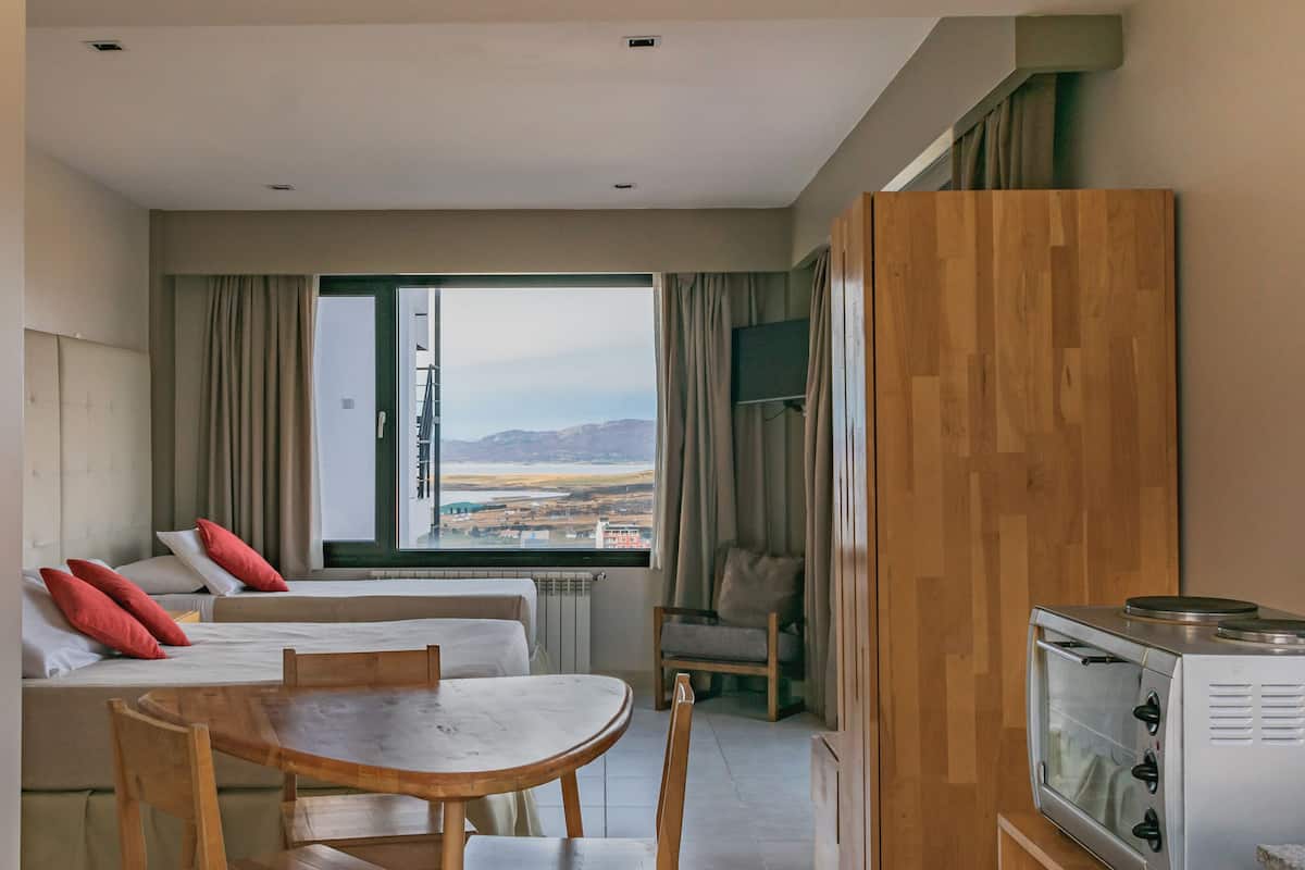 A hotel room with a bed, a dining table, chairs, a TV, and a view of the outdoors.
