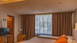 A hotel room with two beds, a TV, a desk, and a window with curtains. - MIRALEJOS APART HOTEL (Ushuaia)