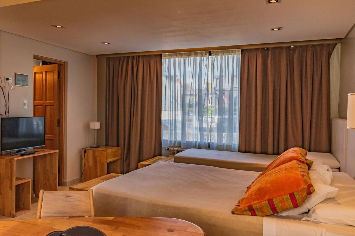 A hotel room with two beds, a TV, a desk, and a window with curtains.