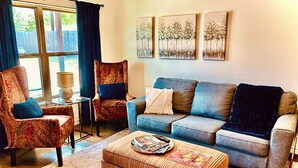 Un salon comprenant un canapé, deux fauteuils, une table basse et un tapis. Trois tableaux sont accrochés au mur.