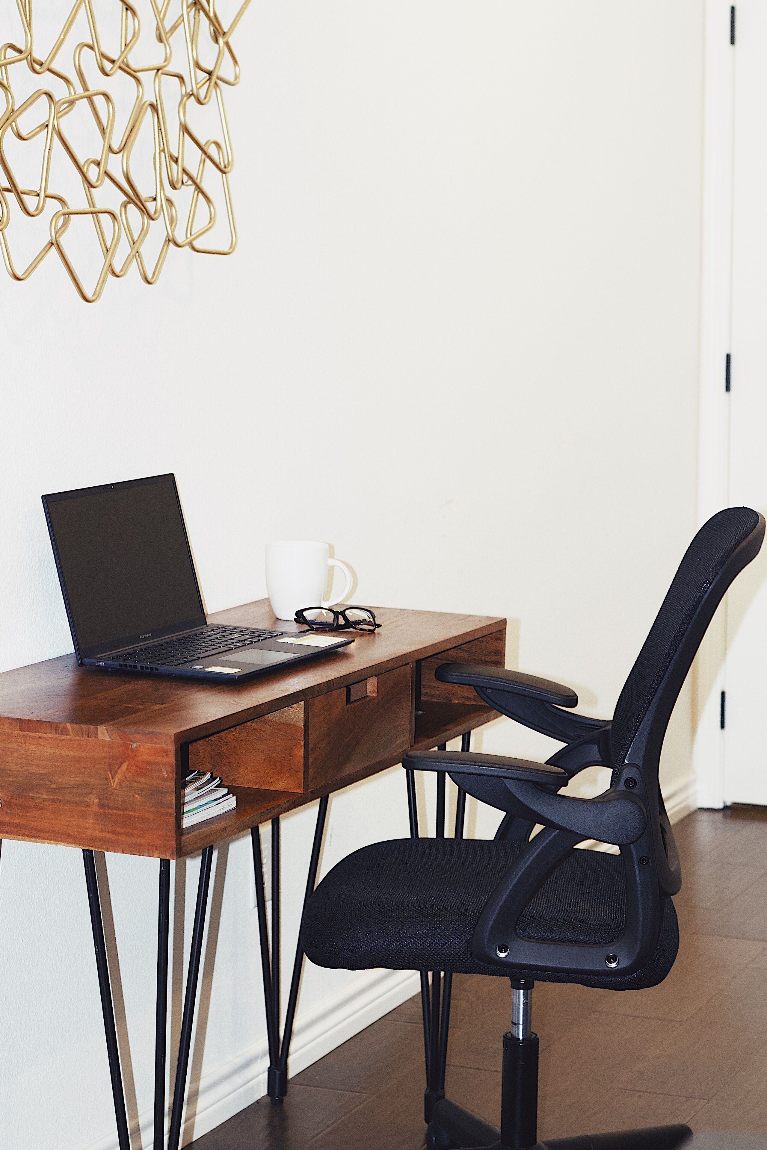 A wooden desk with a laptop, a white mug, and a pair of glasses.