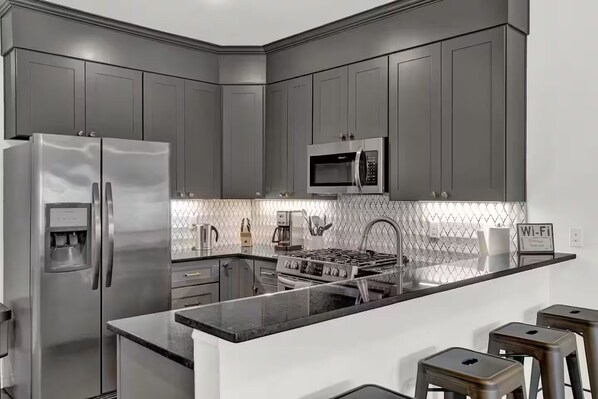 A modern kitchen with grey cabinets, stainless steel appliances, a microwave, and a water dispenser.