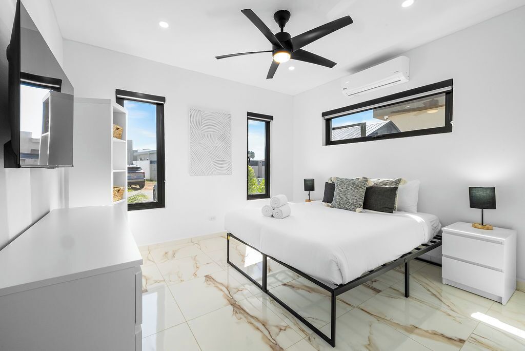 A modern bedroom with a bed, bedside tables, a ceiling fan, and large windows.