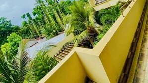 A multi-story building with a staircase leading to a balcony, surrounded by lush greenery and palm trees. - SORENZO Maldives  (Thoddoo)