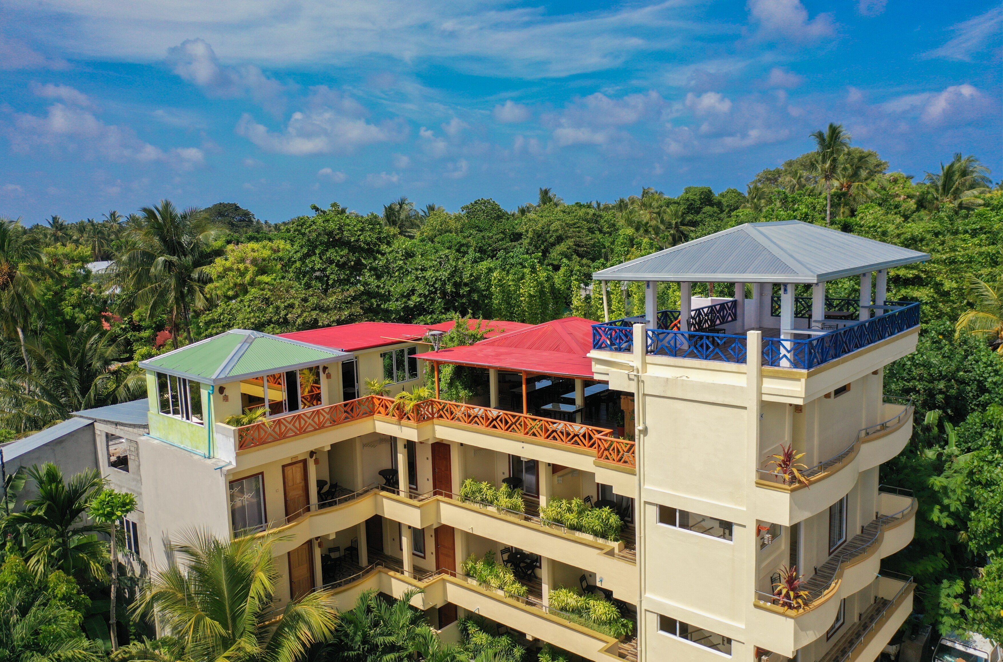 A multi-story building with balconies and a covered terrace area, surrounded by lush greenery.