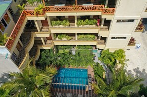 A multi-story hotel with a rooftop pool surrounded by lush greenery and palm trees. - SORENZO Maldives  (Thoddoo)