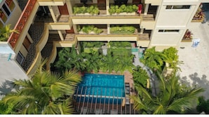 A multi-story hotel with a rooftop pool surrounded by lush greenery and palm trees. - SORENZO Maldives  (Thoddoo)