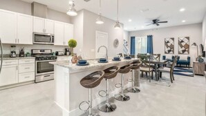 A modern kitchen with white cabinets, stainless steel appliances, and a central island with bar stools. - Amazing home in Orlando just 5 minute away from Disney World (Kissimmee)