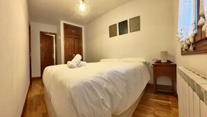A bedroom with a large bed, wooden flooring, a radiator, and a wall-mounted lamp.