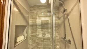 A modern bathroom with a glass shower enclosure, a built-in towel rack, and a small shelf.