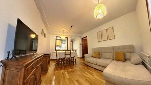 A living room with a television, wooden cabinet, sofa, and a dining area with a table and chairs.