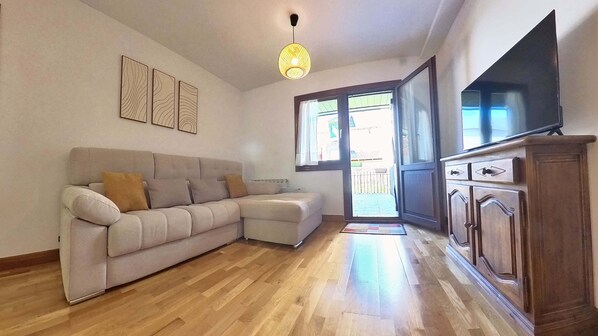 A living room with a sofa, wooden flooring, a TV, and a sliding glass door leading to an outdoor area.
