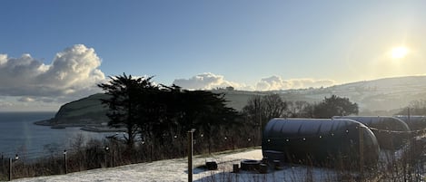 Un paysage enneigé avec une serre, une clôture et une vue lointaine sur la mer et les collines.