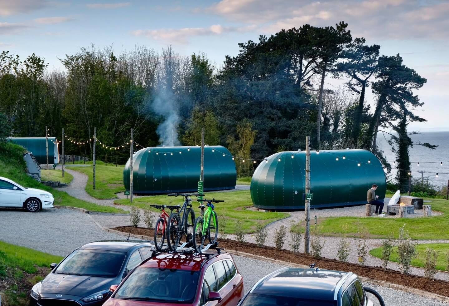 Ein Campingplatz mit grünen, kuppelförmigen Zelten, Fahrrädern davor und einem Auto im Vordergrund.