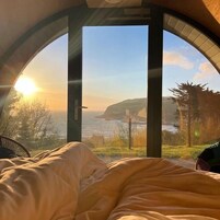 Una cama con vistas al mar y acantilados a través de un gran ventanal en arco.